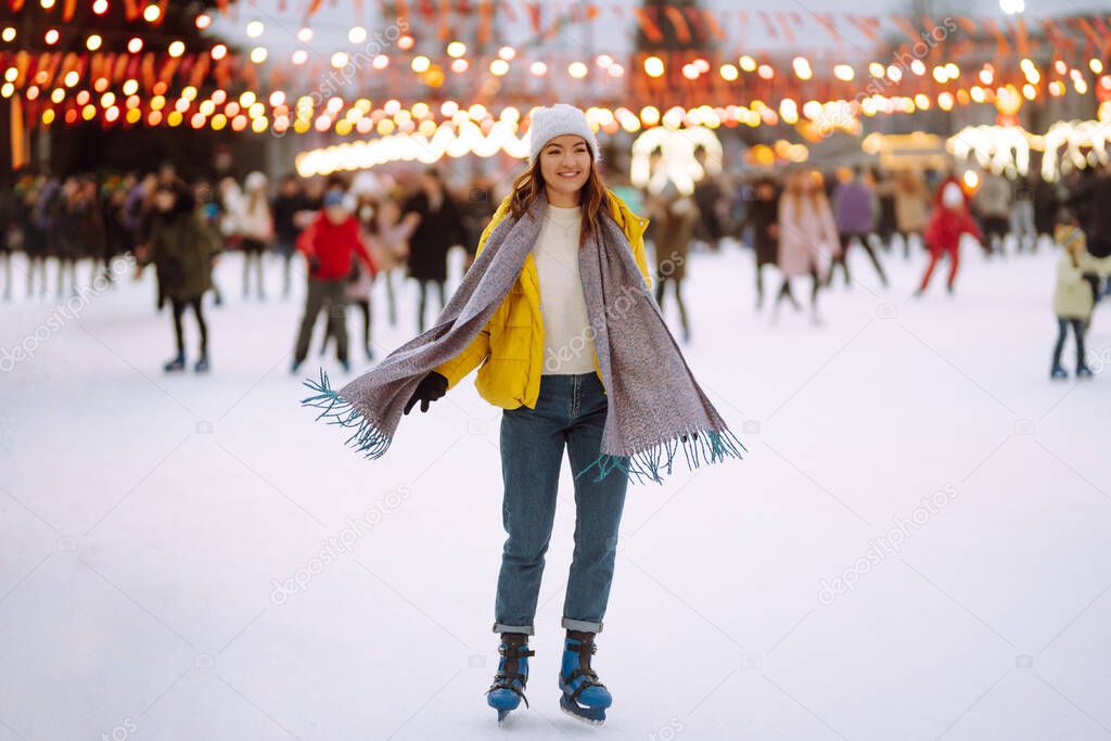 Happy woman ice skating on the ice arena in the city square on Festive Christmas fair. Cold weather. Winter fashion, holidays, active concept.