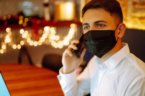 保護顔マスクの若い男はノートパソコンで作業中に自宅で電話で話します 自己分離とコロナウイルスの予防 リモートワーク Covy 2019 テクノロジー ビジネス フリーランスのコンセプト — ストック写真