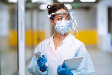 Hastalık kontrol uzmanı vizör ve koruyucu eldiven ve kızılötesi termometre cihazıyla karantinadaki salgın sırasında ofisteki sıcaklığı kontrol ediyor. COVID-19.