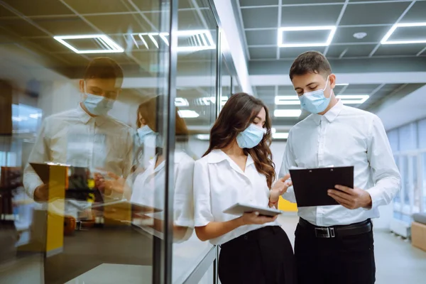 Business colleagues in protective face mask discussing work related matters on an office building hallway. Teamwork during pandemic in quarantine city. Covid-19.