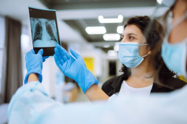 Vizörlü ve koruyucu eldivenli bir kadın doktor röntgen çekmeyi tartışıyor. Doktor, kovid 19 koronavirüs ve pnömoni ışınlarıyla enfekte olmuş bir hastanın akciğerinin röntgenini inceliyor. Florografi.