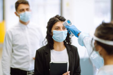 Sıcaklık taraması yapan ofis çalışanları. Hastalık kontrol uzmanı vizör ve koruyucu eldivenler ve kızılötesi termometre cihazıyla karantinadaki salgın sırasında ofisteki sıcaklığı kontrol etmek için. 