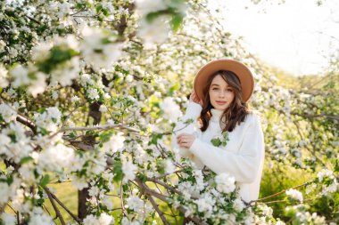 Bahar çiçeklerinde çiçek açan bahçede poz veren genç bir kadın. Kadın güzelliği, moda. Şehir yaşam tarzı.