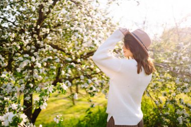 Bahar çiçeklerinde çiçek açan bahçede poz veren genç bir kadın. Kadın güzelliği, moda. Şehir yaşam tarzı.