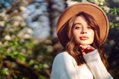 Bahar çiçeklerinde çiçek açan bahçede poz veren genç bir kadın. Kadın güzelliği, moda. Şehir yaşam tarzı.