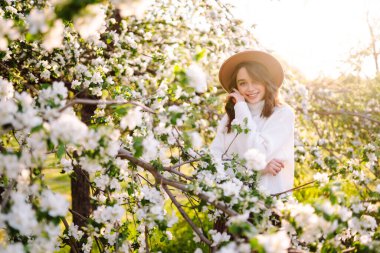 Bahar çiçeklerinde çiçek açan bahçede poz veren genç bir kadın. Kadın güzelliği, moda. Şehir yaşam tarzı.