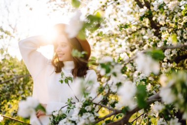 Bahar çiçeklerinde çiçek açan bahçede poz veren genç bir kadın. Kadın güzelliği, moda. Şehir yaşam tarzı.