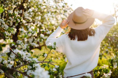 Bahar çiçeklerinde çiçek açan bahçede poz veren genç bir kadın. Kadın güzelliği, moda. Şehir yaşam tarzı.