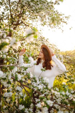 Bahar çiçeklerinde çiçek açan bahçede poz veren genç bir kadın. Kadın güzelliği, moda. Şehir yaşam tarzı.