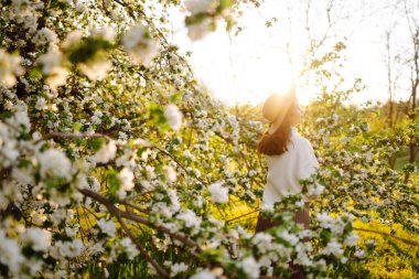 Bahar çiçeklerinde çiçek açan bahçede poz veren genç bir kadın. Kadın güzelliği, moda. Şehir yaşam tarzı.