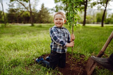Şirin çocuk bahçede büyükbabasıyla birlikte genç bir ağaç diker. Soy ağacı dikiyorum. Bahar konsepti, doğa ve bakım.