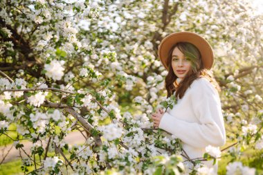 Çiçek açan bahar bahçesinde kokunun tadını çıkaran genç bir kadın. Gençlik, aşk, moda ve yaşam tarzı kavramı.
