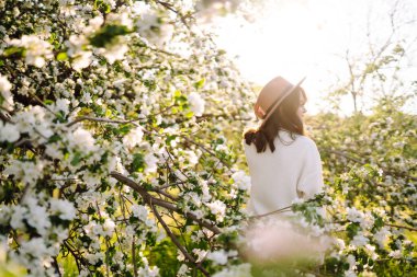 Çiçek açan bahar bahçesinde kokunun tadını çıkaran genç bir kadın. Gençlik, aşk, moda ve yaşam tarzı kavramı.