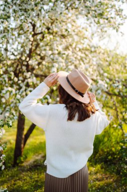 Çiçek açan bahar bahçesinde kokunun tadını çıkaran genç bir kadın. Gençlik, aşk, moda ve yaşam tarzı kavramı.