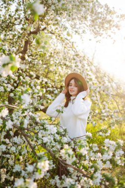 Çiçek açan bahar bahçesinde kokunun tadını çıkaran genç bir kadın. Gençlik, aşk, moda ve yaşam tarzı kavramı.