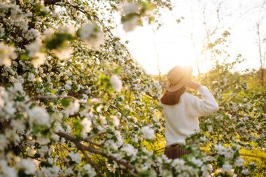Çiçek açan bahar bahçesinde kokunun tadını çıkaran genç bir kadın. Gençlik, aşk, moda ve yaşam tarzı kavramı.