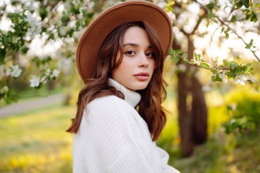 Çiçek açan bahar bahçesinde kokunun tadını çıkaran genç bir kadın. Gençlik, aşk, moda ve yaşam tarzı kavramı.