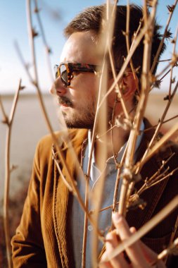 Bahar manzarasında stil yapan adamın portresi. Güneşli bir günde gözlüklü yakışıklı hippi. Gençlik, moda ve yaşam tarzı kavramı..