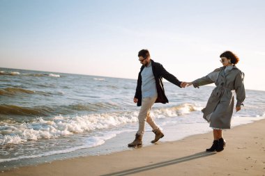 Deniz kenarında yürüyen ve kucaklaşan şık bir çift. Hoş hippi çift birlikte eğleniyor. Gençlik, aşk ve yaşam tarzı kavramı. İlkbahar.