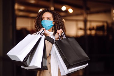 Mağazanın yakınında alışveriş yaptıktan sonra koruyucu maske takan güzel Afro-Amerikan kadın portresi. Coronavirus Covid-19 salgını sırasında alışveriş. Satışlar ve İndirim, Perakende, Satın Alım.