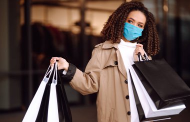 Mağazanın yakınında alışveriş yaptıktan sonra koruyucu maske takan güzel Afro-Amerikan kadın portresi. Coronavirus Covid-19 salgını sırasında alışveriş. Satışlar ve İndirim, Perakende, Satın Alım.