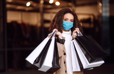 Mağazanın yakınında alışveriş yaptıktan sonra koruyucu maske takan güzel Afro-Amerikan kadın portresi. Coronavirus Covid-19 salgını sırasında alışveriş. Satışlar ve İndirim, Perakende, Satın Alım.