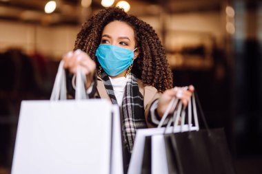 Mağazanın yakınında alışveriş yaptıktan sonra koruyucu maske takan güzel Afro-Amerikan kadın portresi. Coronavirus Covid-19 salgını sırasında alışveriş. Satışlar ve İndirim, Perakende, Satın Alım.