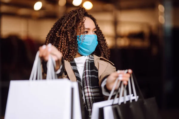 Mağazanın yakınında alışveriş yaptıktan sonra koruyucu maske takan güzel Afro-Amerikan kadın portresi. Coronavirus Covid-19 salgını sırasında alışveriş. Satışlar ve İndirim, Perakende, Satın Alım.
