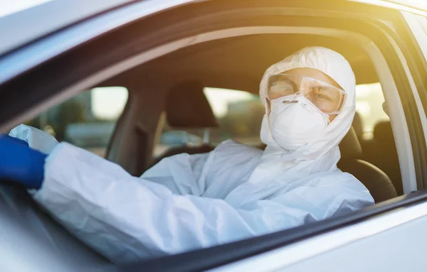 Man in virus protective suit and mask driving car.  Man wearing protective hazmat rides in the car. The concept of preventing the spread of the epidemic, pandemic in quarantine city. Covid -19.
