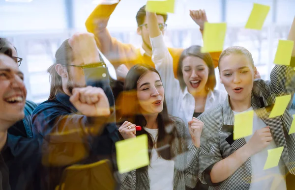 Young business team people brainstorm on corporate project together write strategy tasks on post in sticky notes stand behind glass wall, diverse staff group planning management concept.