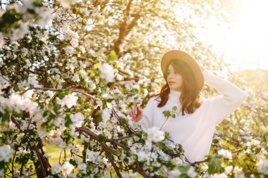 Çiçek açan bahar ağacının yanında güzel genç bir kadın. Gençlik, aşk, moda, romantik ve yaşam tarzı konsepti.