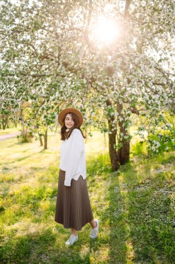 Çiçek açan bahar ağacının yanında güzel genç bir kadın. Gençlik, aşk, moda, romantik ve yaşam tarzı konsepti.