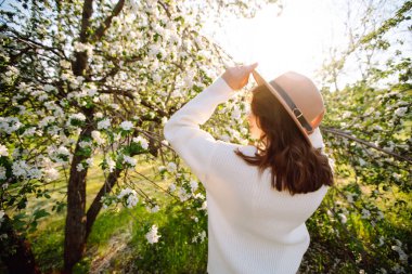Çiçek açan bahar ağacının yanında güzel genç bir kadın. Gençlik, aşk, moda, romantik ve yaşam tarzı konsepti.