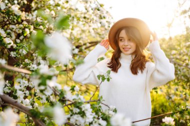 Çiçek açan bahar ağacının yanında güzel genç bir kadın. Gençlik, aşk, moda, romantik ve yaşam tarzı konsepti.