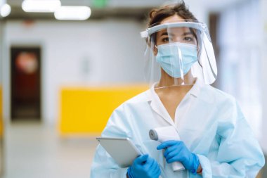 Ofisteki sıcaklığı kontrol etmek için kızılötesi termometre cihazıyla vizör ve koruyucu eldivenler konusunda hastalık kontrol uzmanı. Salgın virüs salgını konsepti. COVID-19.