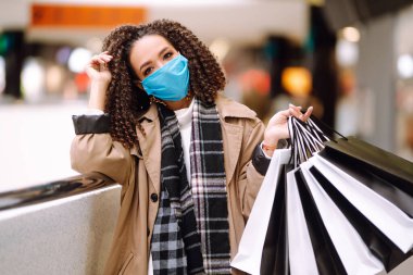 Koruyucu steril tıbbi maskeli Afro Amerikalı kadın alışveriş merkezinden alışveriş yapıyor, alışverişe çıkıyor. Bahar alışverişi. Satın alma, alışveriş, yaşam tarzı konsepti. 