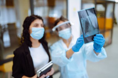 Vizörlü, koruyucu eldivenli bir kadın doktor ve kadın hastanın semptom sorununun röntgenini çeken bir hasta. Zatürree. Işığın röntgenleri. Florografi. Covid 2019.