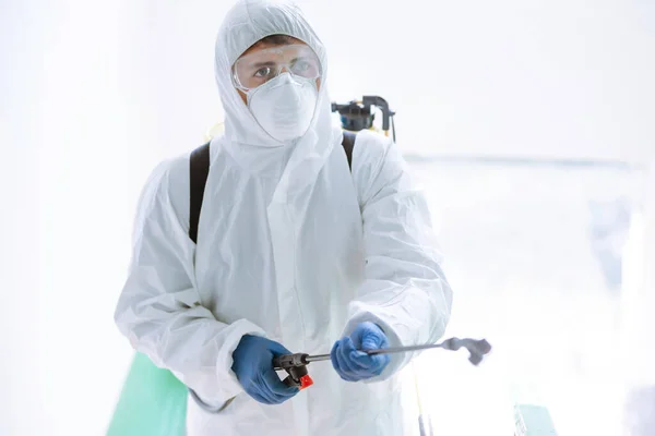 Man in Hazmat suit, protective gloves and goggles use sprayer equipment disinfect  in office. Protection agsinst COVID-19 disease.