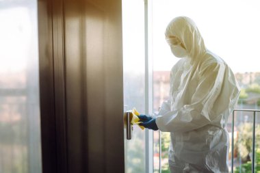 COVID-19 'u önlemek için asansörün temizlenmesi ve dezenfekte edilmesi. Tehlikeli madde giysili bir adam, koruyucu eldivenler ve asansörün dezenfekte düğmeleri. Covid 2019.