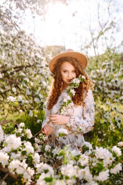 Çiçekli bahar parkında şapkalı mutlu bir kadın. Bahar modası ve yaşam tarzı.