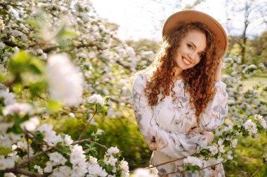 Çiçekli bahar parkında şapkalı mutlu bir kadın. Bahar modası ve yaşam tarzı.