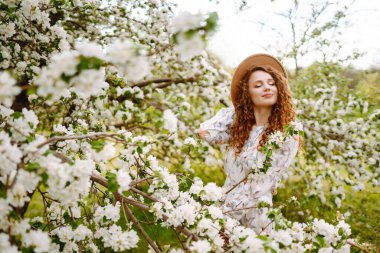 Çiçekli bahar parkında şapkalı mutlu bir kadın. Bahar modası ve yaşam tarzı.