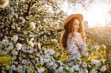 Çiçekli bahar parkında şapkalı mutlu bir kadın. Bahar modası ve yaşam tarzı.
