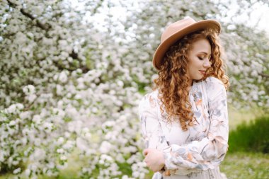 Çiçekli bahar parkında şapkalı mutlu bir kadın. Bahar modası ve yaşam tarzı.