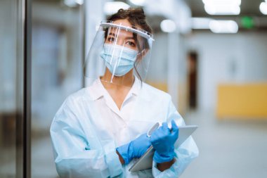 Ofisteki sıcaklığı kontrol etmek için kızılötesi termometre cihazıyla vizör ve koruyucu eldivenler konusunda uzman. Covid 19.