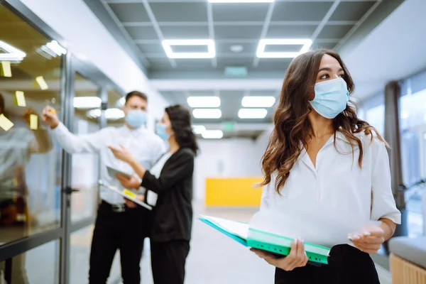 Young business woman in protective face mask an office building hallway. Teamwork of Business people during pandemic of coronavirus. Covid-19.