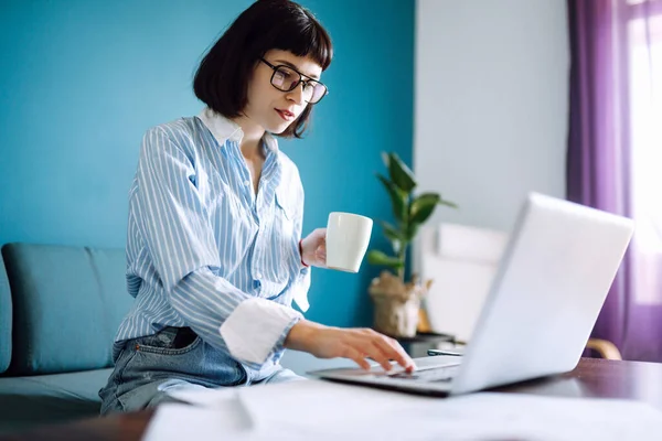 Mulher Bonita Trabalhando Computador Portátil Enquanto Sentado Sala Estar Bebendo — Fotografia de Stock