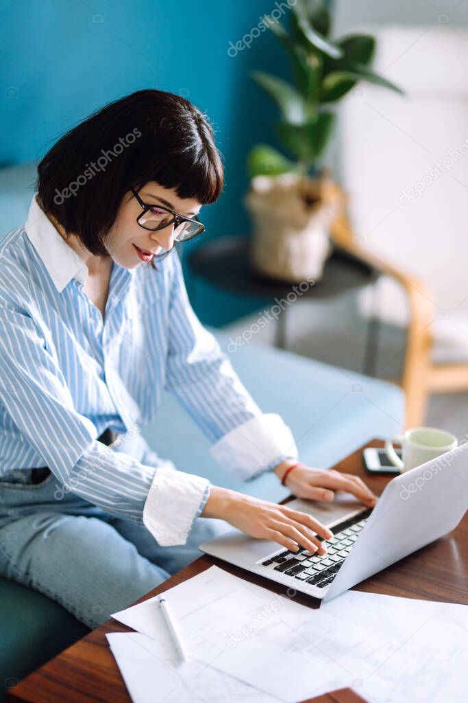 Beautiful  woman working on laptop computer while sitting at the living room, drinking coffee. Technology, freelance, shopping online, remote work, E learning concept. 