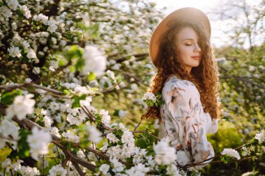 Lanet bahar parkında poz veren şapkalı kıvırcık kadın. Rahatlama, seyahat, cennet, romantizm ve bahar tatili kavramı. Moda tarzı.
