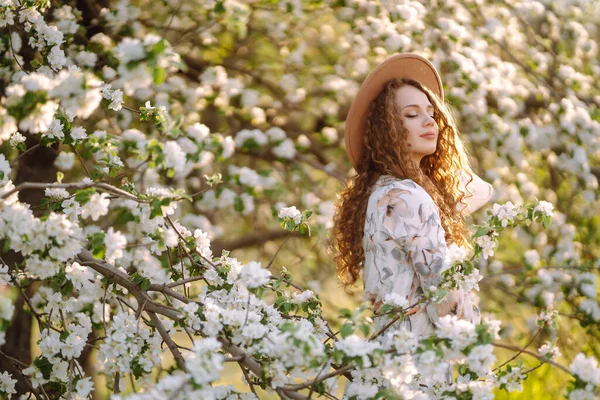 Kręcona Kobieta Kapeluszu Pozująca Kwitnącym Wiosennym Parku Koncepcja Relaksu Podróży — Zdjęcie stockowe